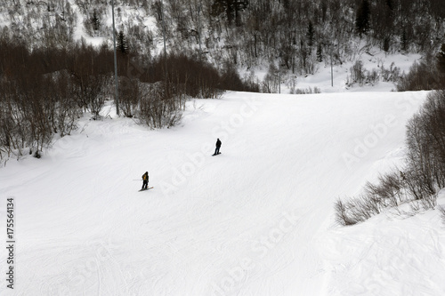 Skier and snowboarder downhill on ski slope at gray winter day