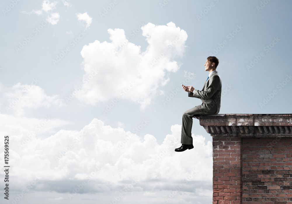 Man on roof edge reading book and cityscape at background Man on roof edge reading book and cityscape at background