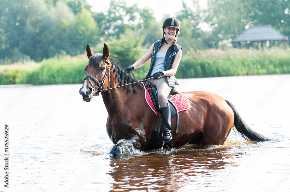 Smililng young teenage girl riding horseback in river