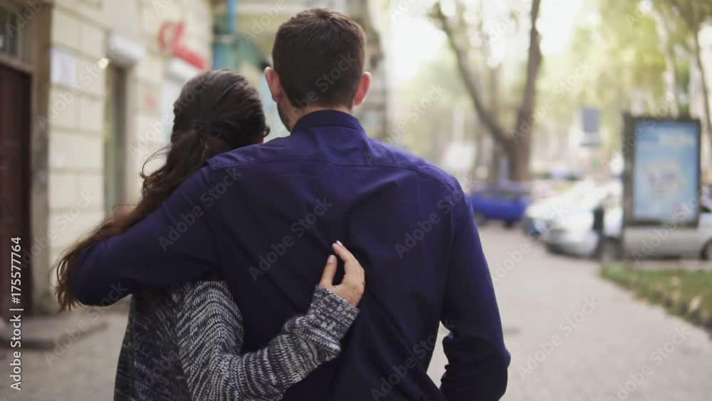 Close-up back view of young beautiful couple walking in the street embracing each other and talking. Romantic date Close-up back view of young beautiful couple walking in the street embracing each other and talking. Romantic date