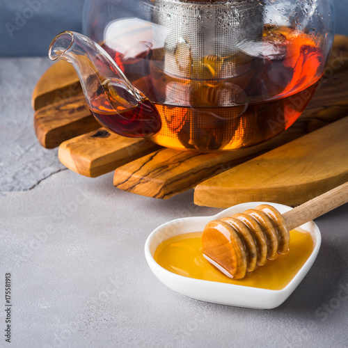 Red tea rooibos and honey in glass teapot on gray