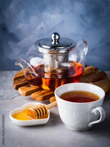 Cup of red tea rooibos and honey with glass teapot on blue