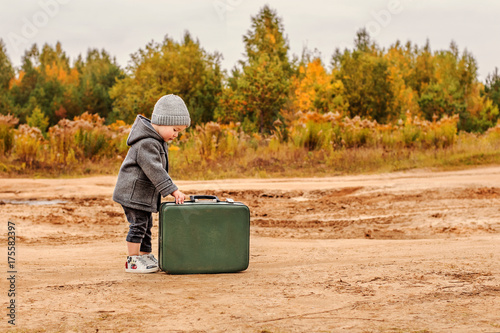 cute little boy opens an old green suitcase in retro clothes