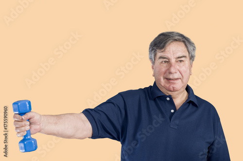 Senior man in a gym class doing Pilates exercise lift weights over a pastel color background