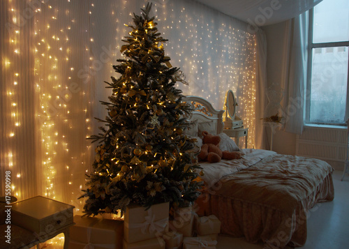 Interior of the bedroom, prepared for the New Year and decorated with a Christmas tree and gifts. Luminous garlands hang on the wall.