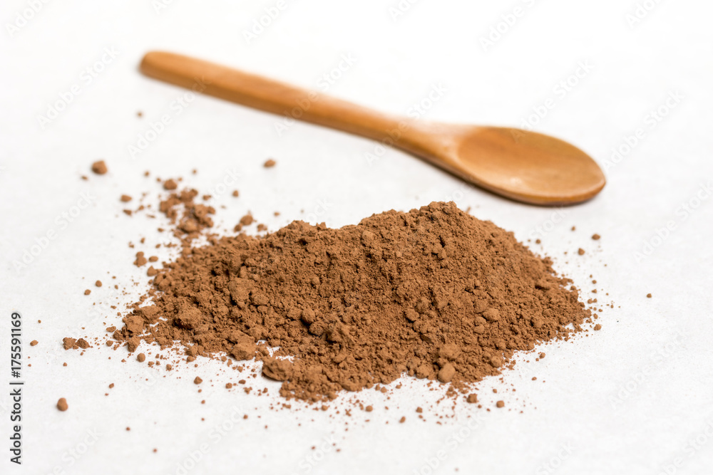 Brown cocoa powder with wooden spoon isolated above white marble background Brown cocoa powder with wooden spoon isolated above white marble background