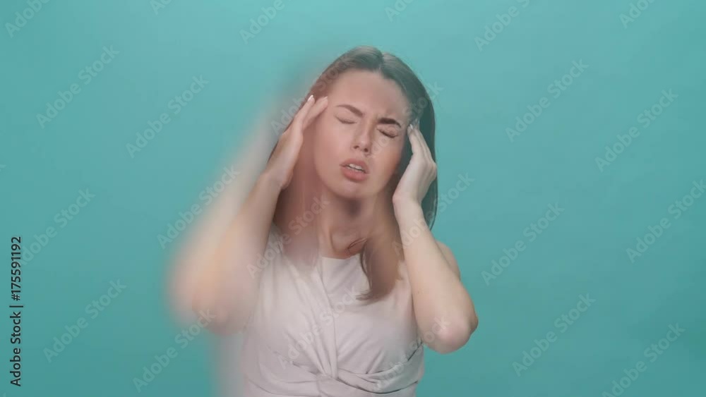 Upset brunette woman in t-shirt with throbbing headache over turquoise background Upset brunette woman in t-shirt with throbbing headache over turquoise background