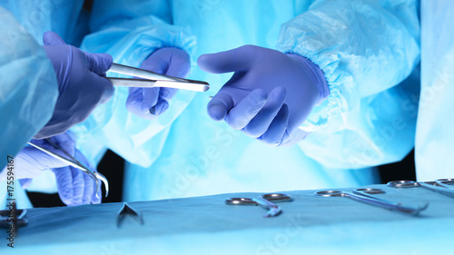 Surgeons hands holding surgical scissors and passing surgical equipment, close-up. Health care and veterinary concept