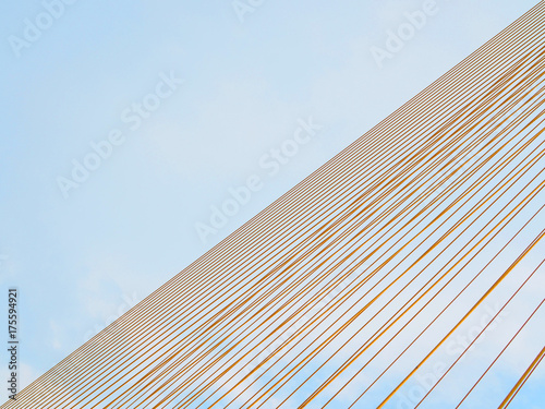 Yellow suspension bridge cable diagonally stacked with the other half of blue bright cloudy sky area, abstract background