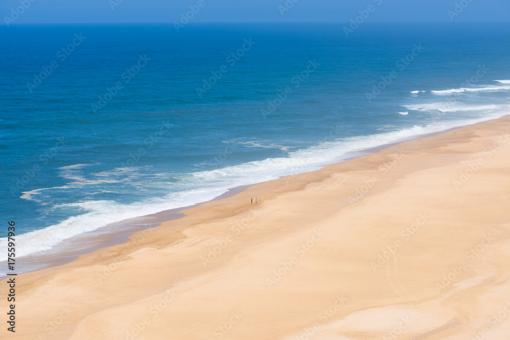 Aeria view of wide empty sandy beach with deep blue ocean clear sky and two people standing on the shore in Portugal