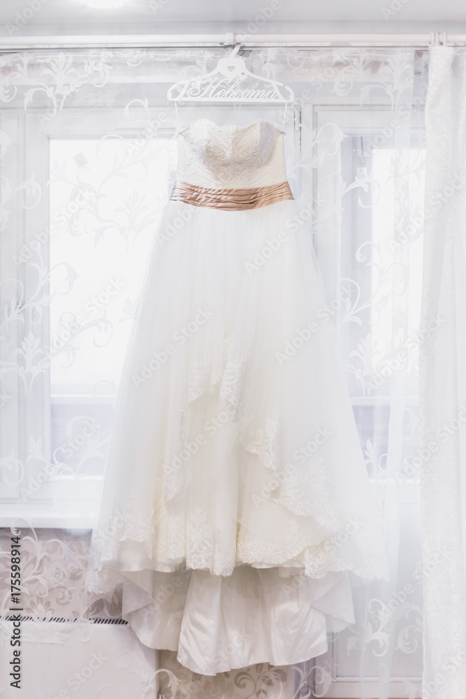 Beautiful white wedding dress hanging by window Beautiful white wedding dress hanging by window