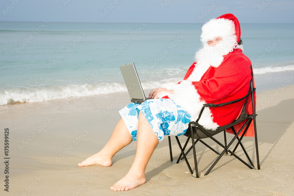 Funny Santa on the beach working on laptop. 