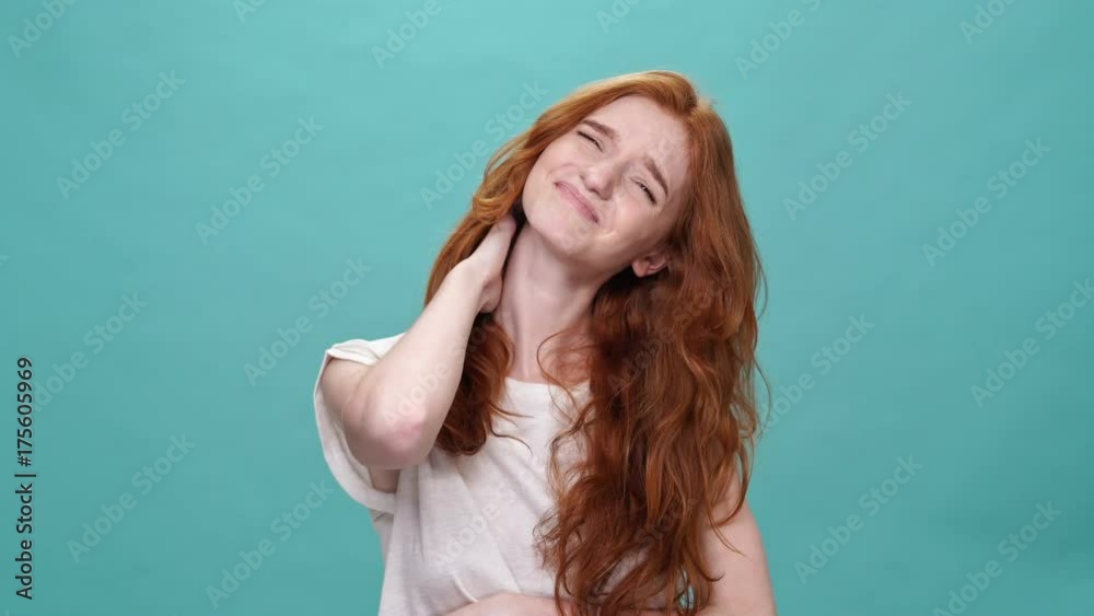 Confused ginger woman in t-shirt itches whole body and looking at the camera over turquoise background Confused ginger woman in t-shirt itches whole body and looking at the camera over turquoise background
