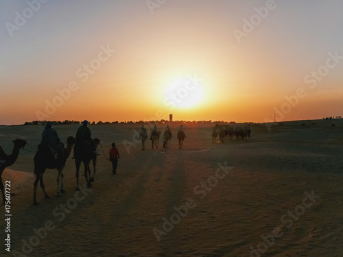 Tourists and bedouins on camels meet sunset in Sahara desert. Tunisia.