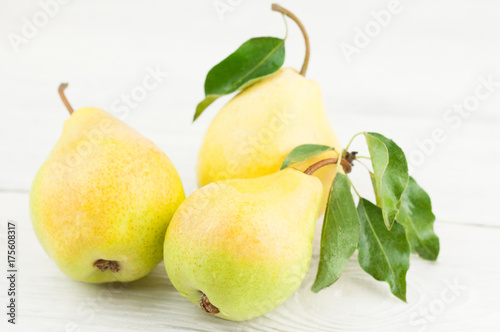Three fresh whole ripe pears with green leafs on old rustic white wooden table