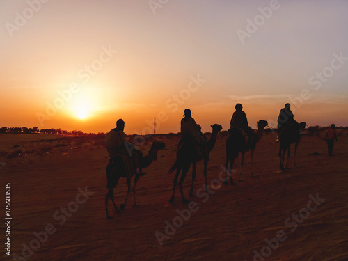 Tourists and bedouins on camels meet sunset in Sahara desert. Tunisia