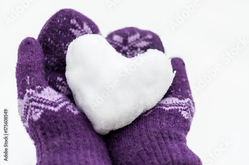 female hands in warm knitted mittens keep the heart from snow against the background of white snow