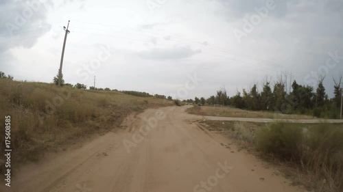 A view of the rural dirt road from camera installed on back of the car driving along this country road. Riding on a rough roadway. Traces of tires on the sand.