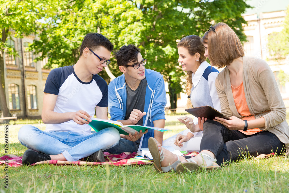Group of young people discuss and talk. Students sitting on a clearing in the campus. Group of young people discuss and talk. Students sitting on a clearing in the campus.