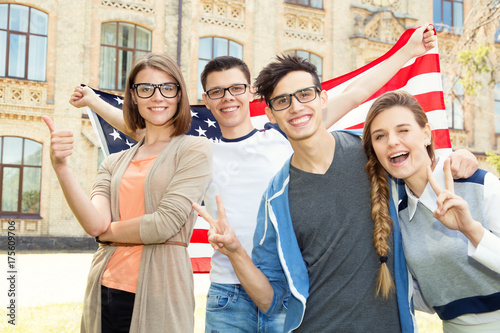 Group of students holding flag of USA on the university campus. Group four happy people having waving American flag. Vote United States, election.