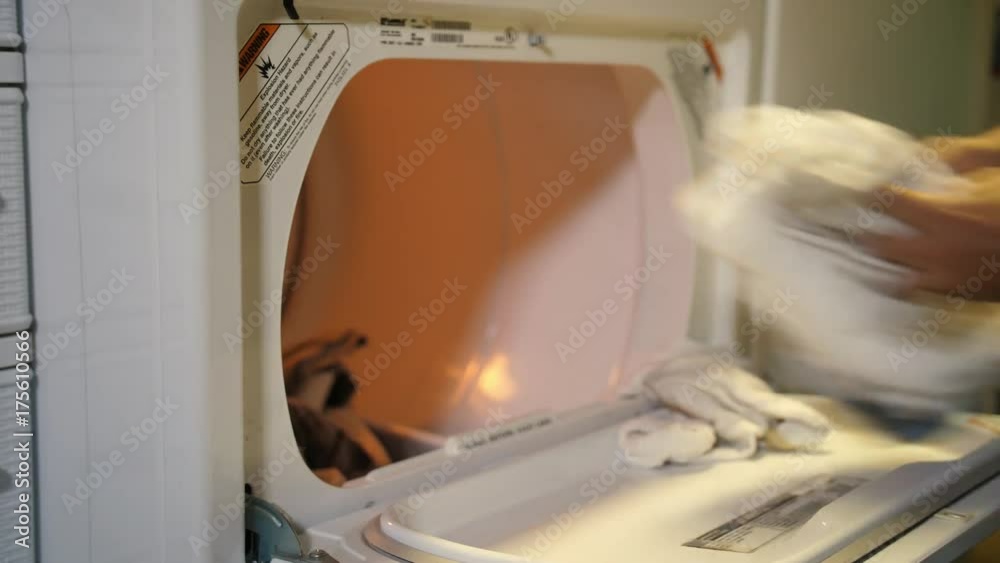 A man puts a load of laundry in the drier. Shallow DOF. Shot at 60fps