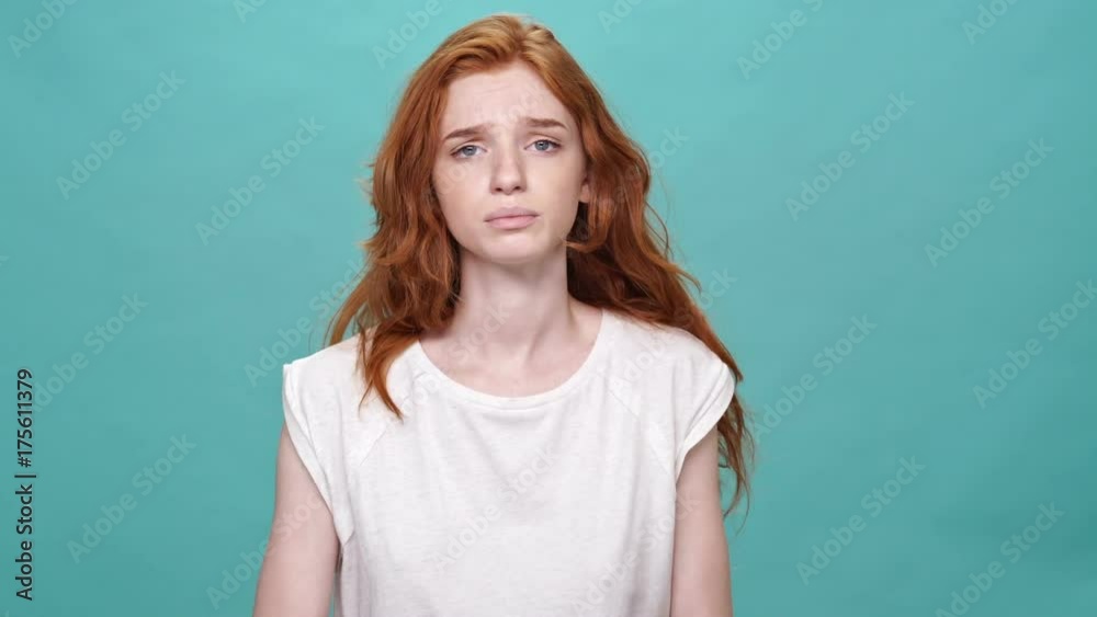 Upset ginger woman in t-shirt asks something while showing over turquoise background Upset ginger woman in t-shirt asks something while showing over turquoise background