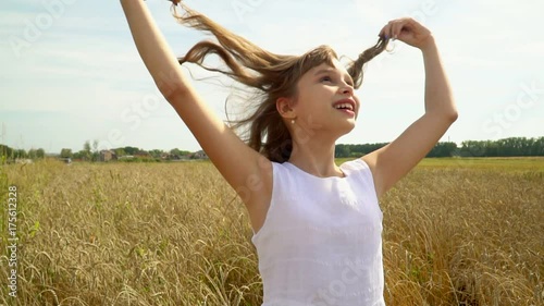 The girl in a white dress goes across the field of gold wheat. The beautiful girl enjoys open spaces of the Russian fields. The girl walks across the field of ripe wheat and smiles. Slow motion photo