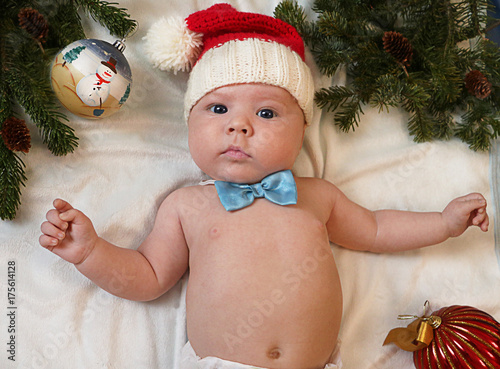 Baby first christmas. Beautiful little baby in Santa hat and bow tie lays on white background framed with christmas tree needles and balls. New Year's holidays. Santa baby.
