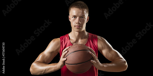 Basketball player hold a basketball ball. Isolated basketball player on a black background. Player wears unbranded clothes. © Alex