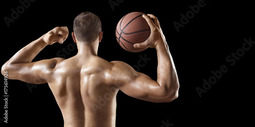 Basketball player hold a basketball ball. Isolated basketball player on a black background. Basketball player with a naked torso and pumped muscles.