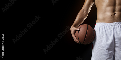 Basketball player hold a basketball ball. Isolated basketball player on a black background. Basketball player with a naked torso and pumped muscles. © Alex
