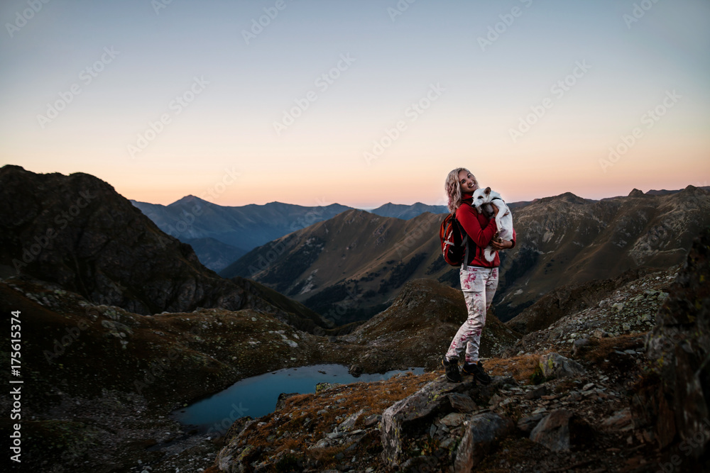 Girl hiker with dog standing on a brink rock and looking at the mountains
