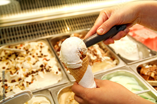Female hand with scoop takes ice cream from the fridge and serving in waffle cone. Woman taking scoop of tasty ice cream. Fridge with ice cream. Woman works in ice cream shop. Pastry shop. Desserts.
