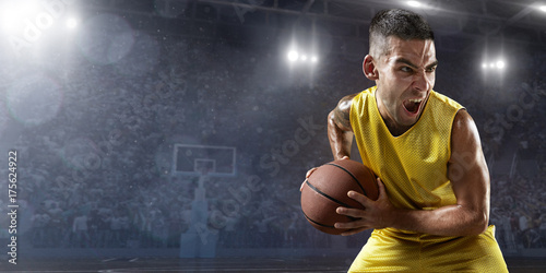 Basketball player hold a basketball ball on big professional arena. Player is preparing to throw the ball and emotionally shouts. Player wears unbranded clothes.