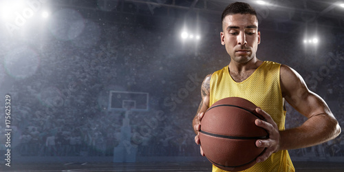 Basketball player hold a basketball ball on big professional arena. Player wears unbranded clothes.