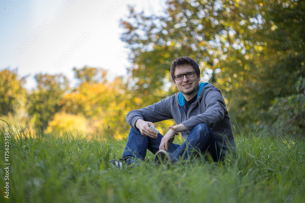 Junger Mann sitzt im Gras, Smartphone, entspannt und nachdenklich, Textfreiraum Junger Mann sitzt im Gras, Smartphone, entspannt und nachdenklich, Textfreiraum
