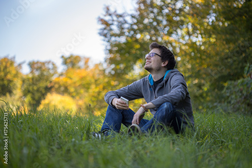 Junger Mann sitzt im Gras, Smartphone, entspannt und nachdenklich, Textfreiraum