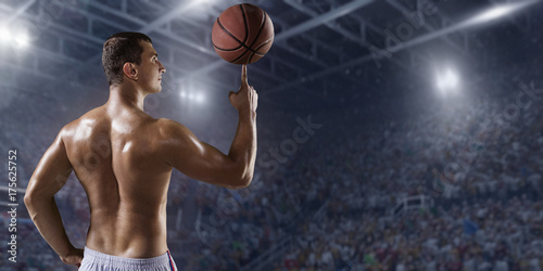 Basketball player hold a basketball ball on big professional arena. Basketball player with a naked torso and pumped muscles. Player wears unbranded clothes.