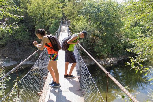 Travelers travel on the suspension bridge go trekking together. Active hikers. Trekking together. Eco tourism and healthy lifestyle concept. Two Tourists With Backpacks travel