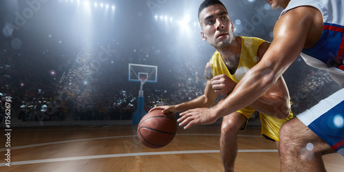 Two basketball players fight for the basketball ball on big professional arena. Player wears unbranded clothes.