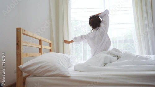 Closeup alarm clock, rear view Young asian woman wake up in the morning and sitting on bed at mirror door side relaxing in holiday with sunlight, snooze sleeping photo