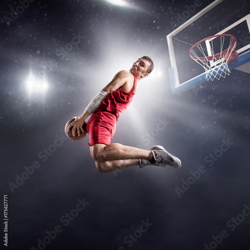 Basketball player makes slam dunk on big professional arena. Player flies through the air with the ball. Player wears unbranded clothes.