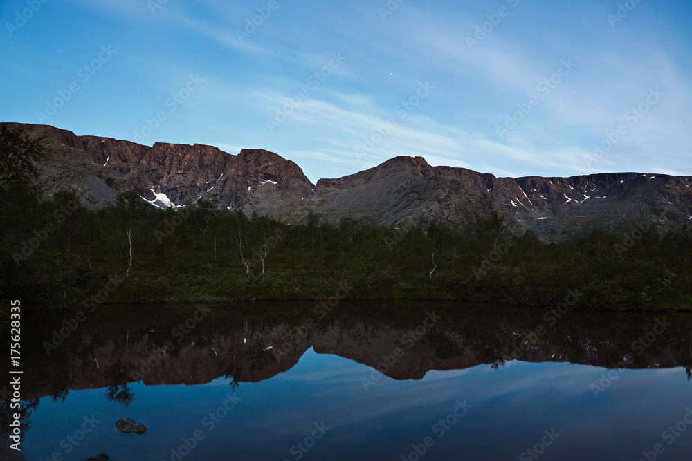 The sky with the stars at dawn, reflected in the water of a mountain lake.