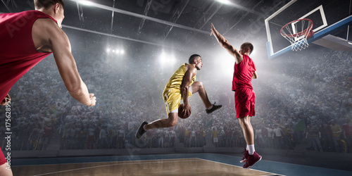 Basketball player makes slam dunk on big professional arena. Player flies through the air with the ball. Opponents try to prevent the ball from hitting the basketball ring. © Alex