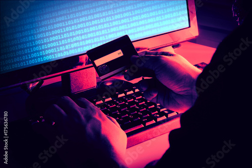 Black hands of anonymous hackers holding credit card and using, typing code on keyboard of laptop for remotely reach, receiving personal information online, Networking Crime Payment Security Concept