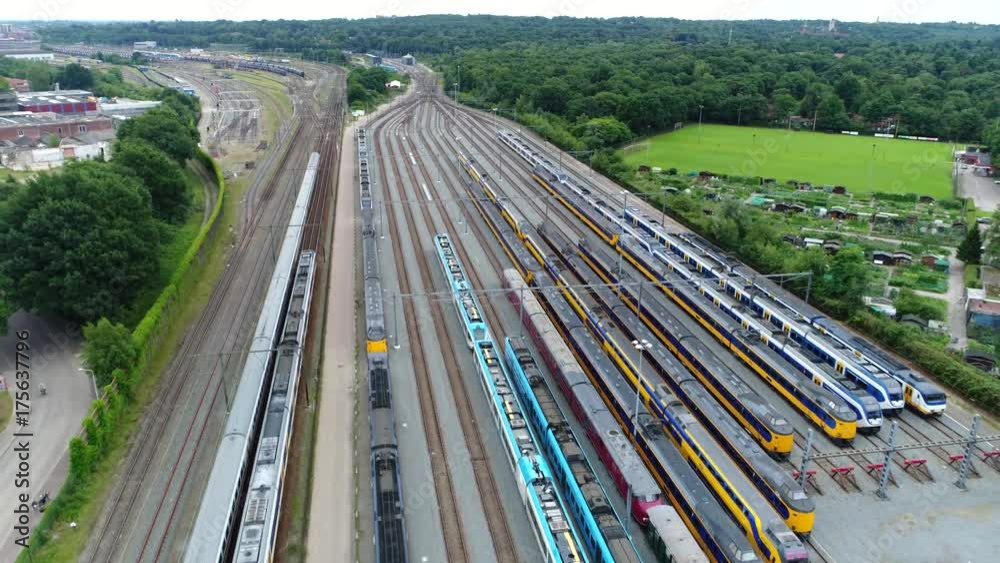 Aerial of railroad hub or railway terminal flying backwards showing trains passing by fast also showing different trains parked next to each other on the rail tracks 4k high resolution footage