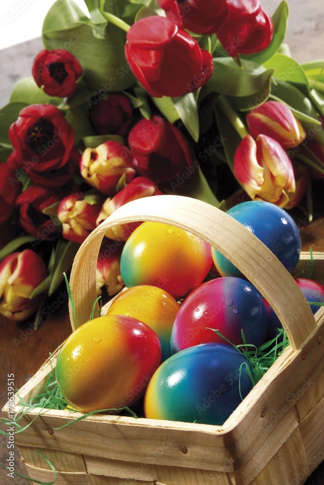 Basket filled with coloured eggs, a bunch of tulips in background Basket filled with coloured eggs, a bunch of tulips in background