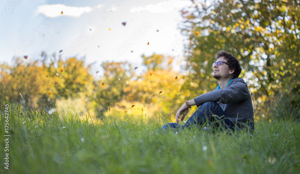 Fototapeta premium Junger Mann sitzt im Gras, tanzende Blätter, Textfreiraum, Breitbild