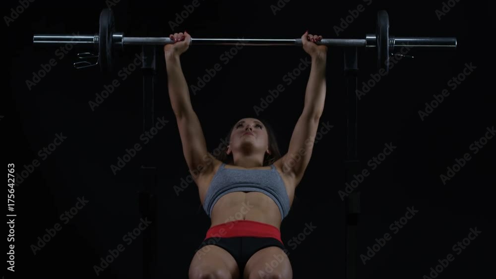 Fit young woman weight training, doing bench press with barbell Fit young woman weight training, doing bench press with barbell