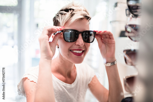 Beautiful middle age woman choosing a glasses in optician store.